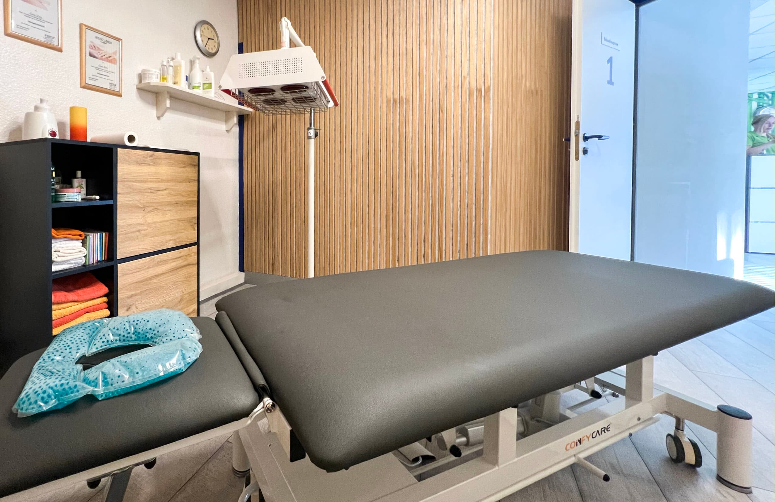 Behandlungsraum mit Therapieliege, Wärmelampe und Holz-Akustikwand